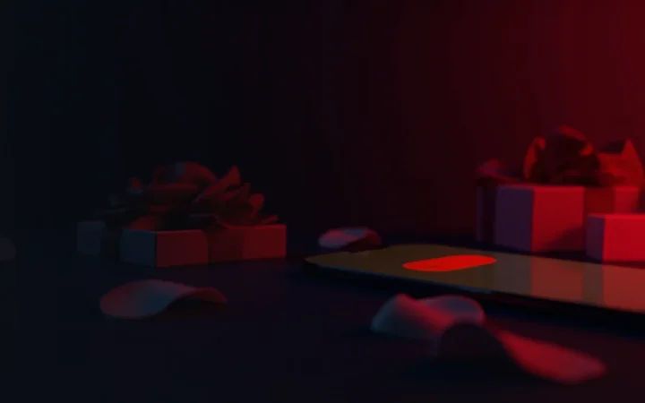 A dark navy desk with a glowing red chat bubble on a phone, a blank gift box and rose petals, leaving the left side empty.