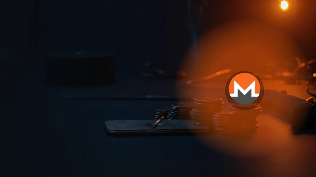 The Monero logo over a dark navy background of blank metal coins, a steel plate and a black device lit in orange.