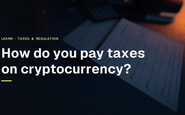 The title How do you pay taxes on cryptocurrency? over a dark desk with blank tax forms, a calculator, a pen and a folder under warm orange light.