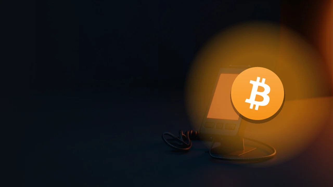 Bitcoin-logoet over et mørkt skrivebord med en tom glødende kortlæser og orange lys.