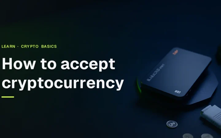 How to accept cryptocurrency title over a dark desk with a blank terminal, a hardware wallet and coins in lime green light.