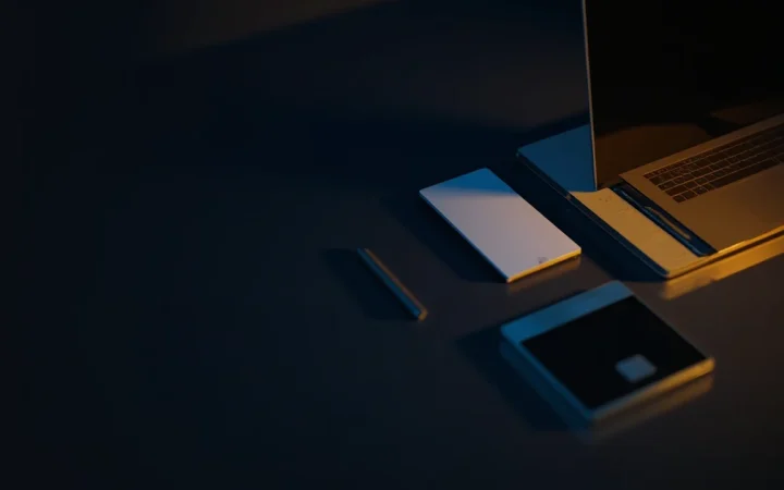 Et mørkt skrivebord med en laptop, papirer og en telefon oplyst af guldlys.