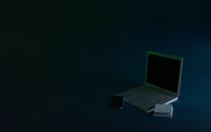 A dark desk with a laptop, phone and blank cards, lit by a lime green glow.