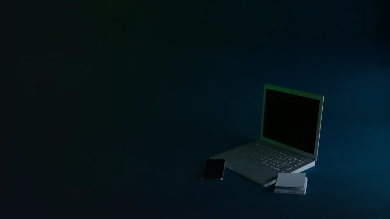 Ett mörkt skrivbord med en laptop, telefon och tomma kort, upplyst av ett limegrönt sken.