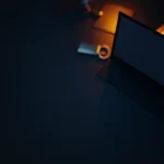 Et mørkt navy-skrivebord med en hardware wallet, stålplade, hængelås og skjold oplyst af orange glød.