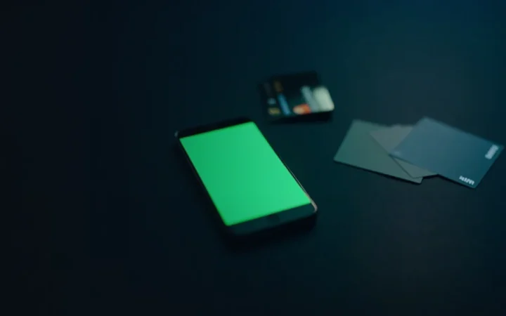 A dark desk with a glowing phone, a hardware wallet and blank payment cards.