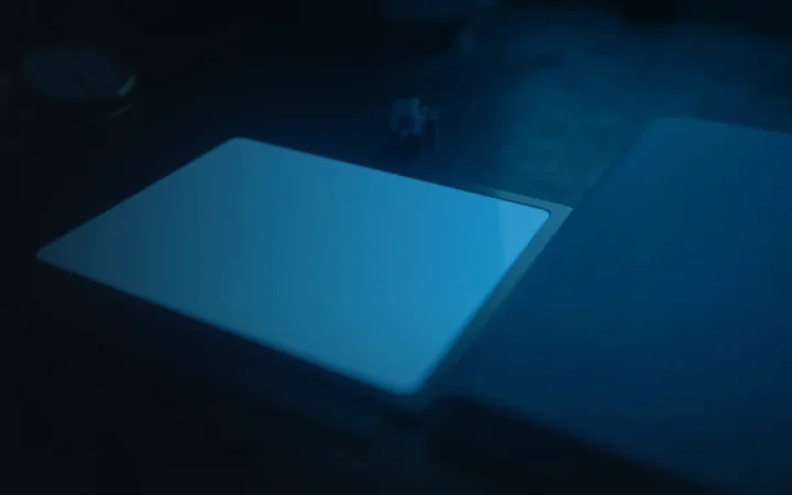 Et mørkt skrivebord med en lysende tablet, mappe og ur.