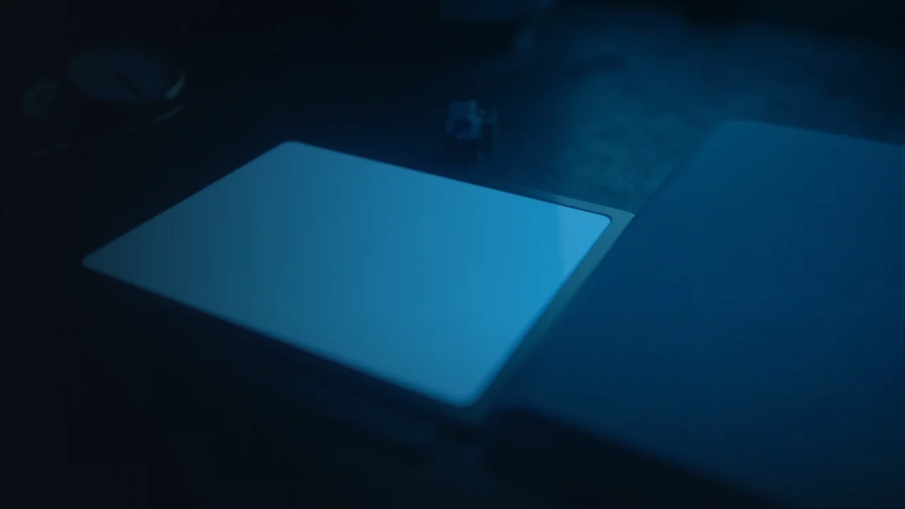Et mørkt skrivebord med en lysende tablet, mappe og ur.