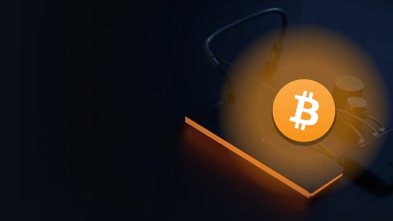 Bitcoin-logoet over et mørkt skrivebord med et glødende kabel og en enhed med tom skærm.