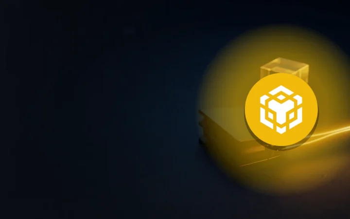BNB-logoet over et mørkt skrivebord med en wallet og glødende guldkabler.