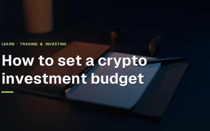 Titlen How to set a crypto investment budget over et mørkt marineblåt skrivebord med en lukket mappe, et tomt notesblok og en pen oplyst af orange glød.