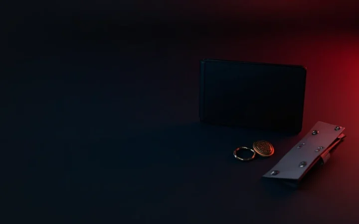 Et mørkt skrivebord med en hardware-wallet, stålplade, hængelås og skjoldmærke i rødt lys.