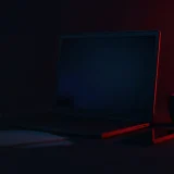 Et mørkt skrivebord med en tom laptop, telefon, papir og konvolut oplyst af rødt lys.