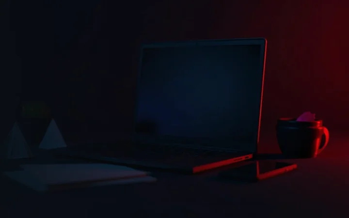 Et mørkt skrivebord med en tom laptop, telefon, papir og konvolut oplyst af rødt lys.