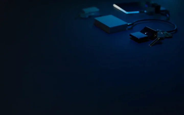 Et mørkt skrivebord med et glødende blåt kabel, en blank smartphone, en blank terminal, blanke kort og en metalkey.