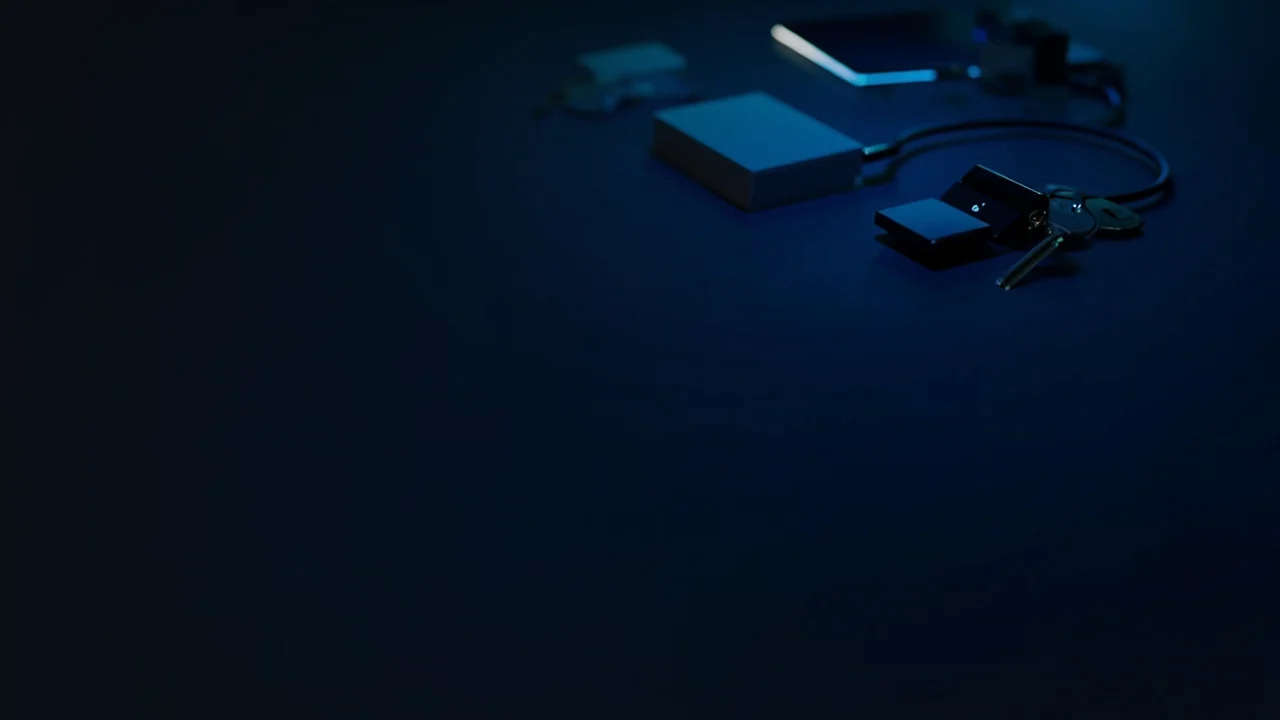 Et mørkt skrivebord med et glødende blåt kabel, en blank smartphone, en blank terminal, blanke kort og en metalkey.