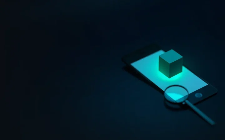 The with a dark navy background of a phone, glowing cube and magnifying glass.