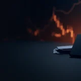 A dark desk with a blank phone, blank cards and a glowing orange chart.