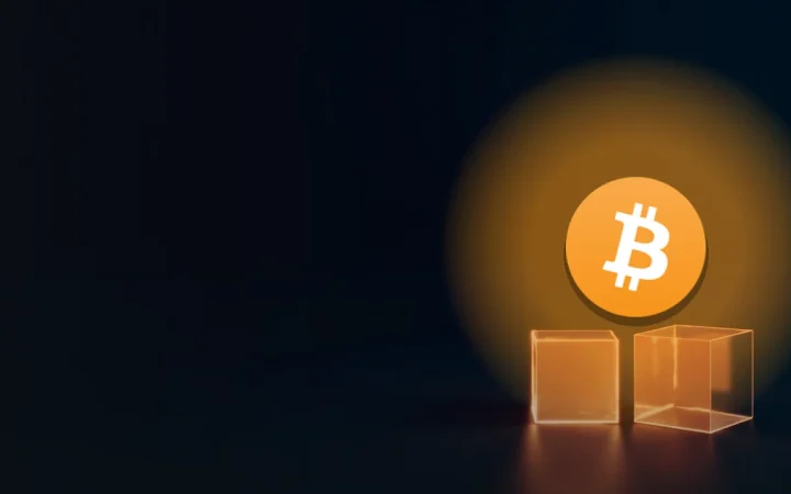 Bitcoin-logoet over en mørk navyblå baggrund med en glødende glaskube og en mindre metalkube.