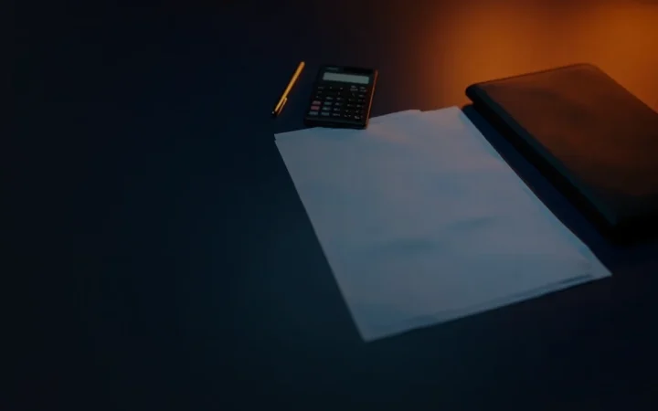 Dark navy scene with blank forms, a calculator and a pen lit by warm orange glow.