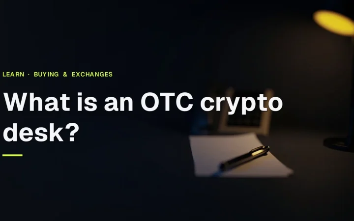 Titlen What is an OTC crypto desk? over et mørkt bord med en telefon, blanke papirlapper og en pen oplyst i guld.