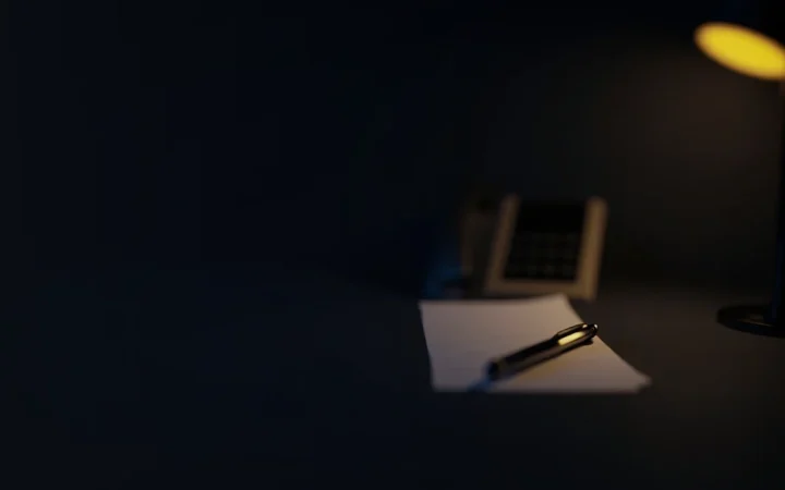 Et mørkt skrivebord med en telefon, blanke papirsedler og en pen oplyst i guld.