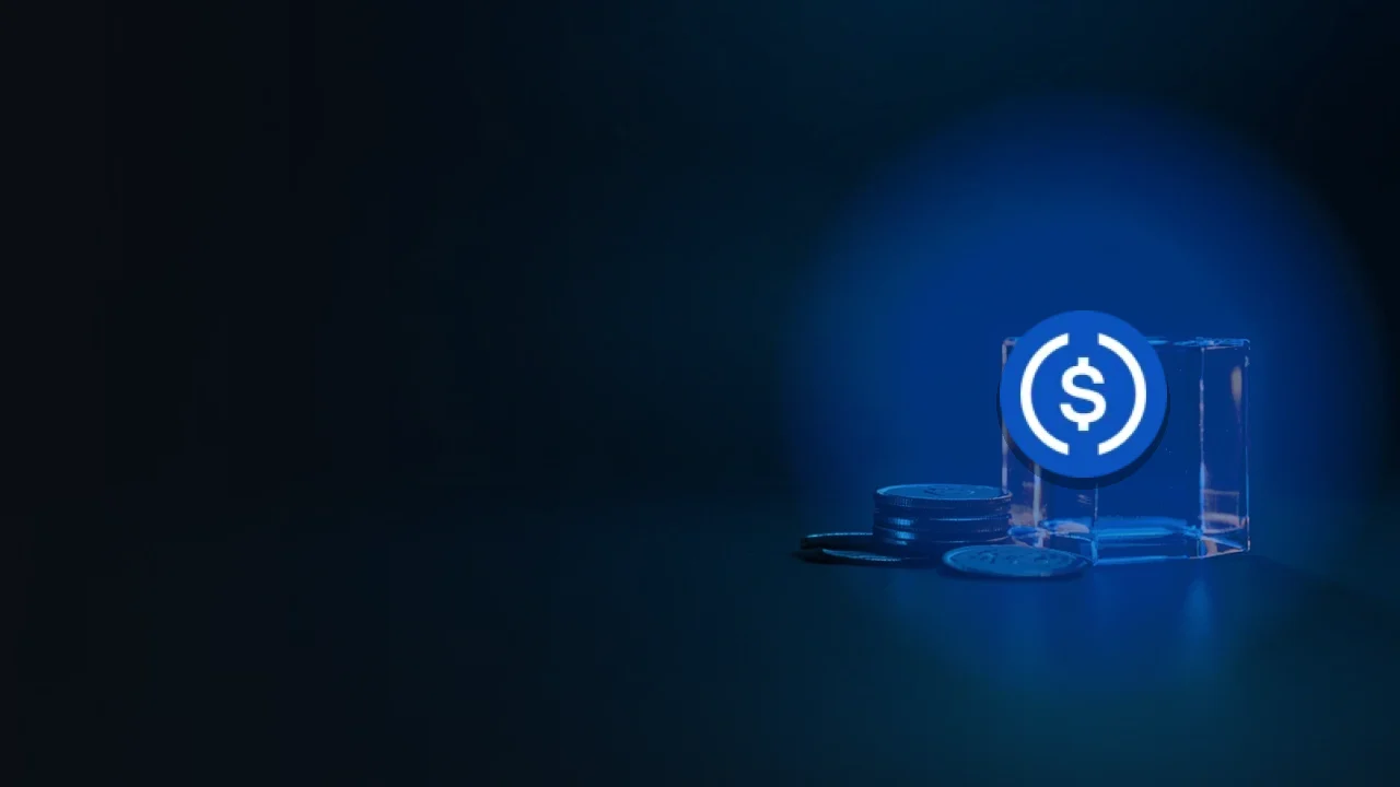 暗いネイビーの背景に、無地の銀貨と青い光に照らされたガラスの金庫、その上にUSD Coinのロゴ。