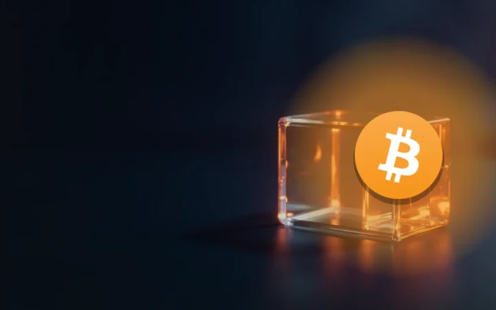 The Bitcoin logo over glass blocks joined by glowing orange light on a dark navy background.