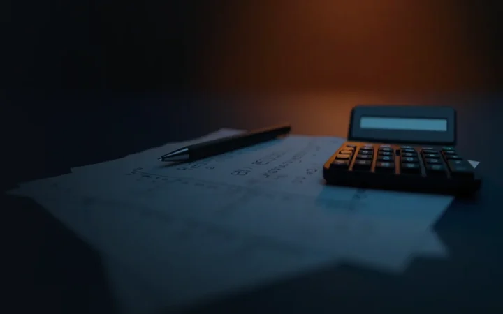 A dark desk with blank forms, a calculator and a pen.